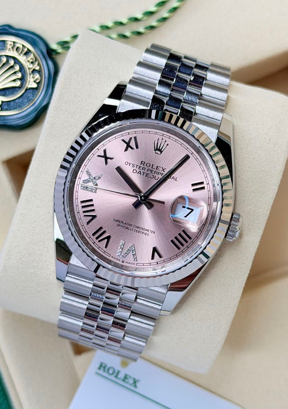 Rolex Datejust 36 126234 White Rolesor, pink Roman dial, diamond accents on Jubilee bracelet, angled front view beside a green Rolex seal