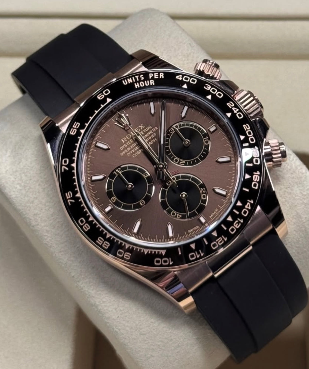 A close-up of a Rolex Daytona watch with a chocolate dial, rose gold case, black cerachrome bezel, and black Oysterflex strap
